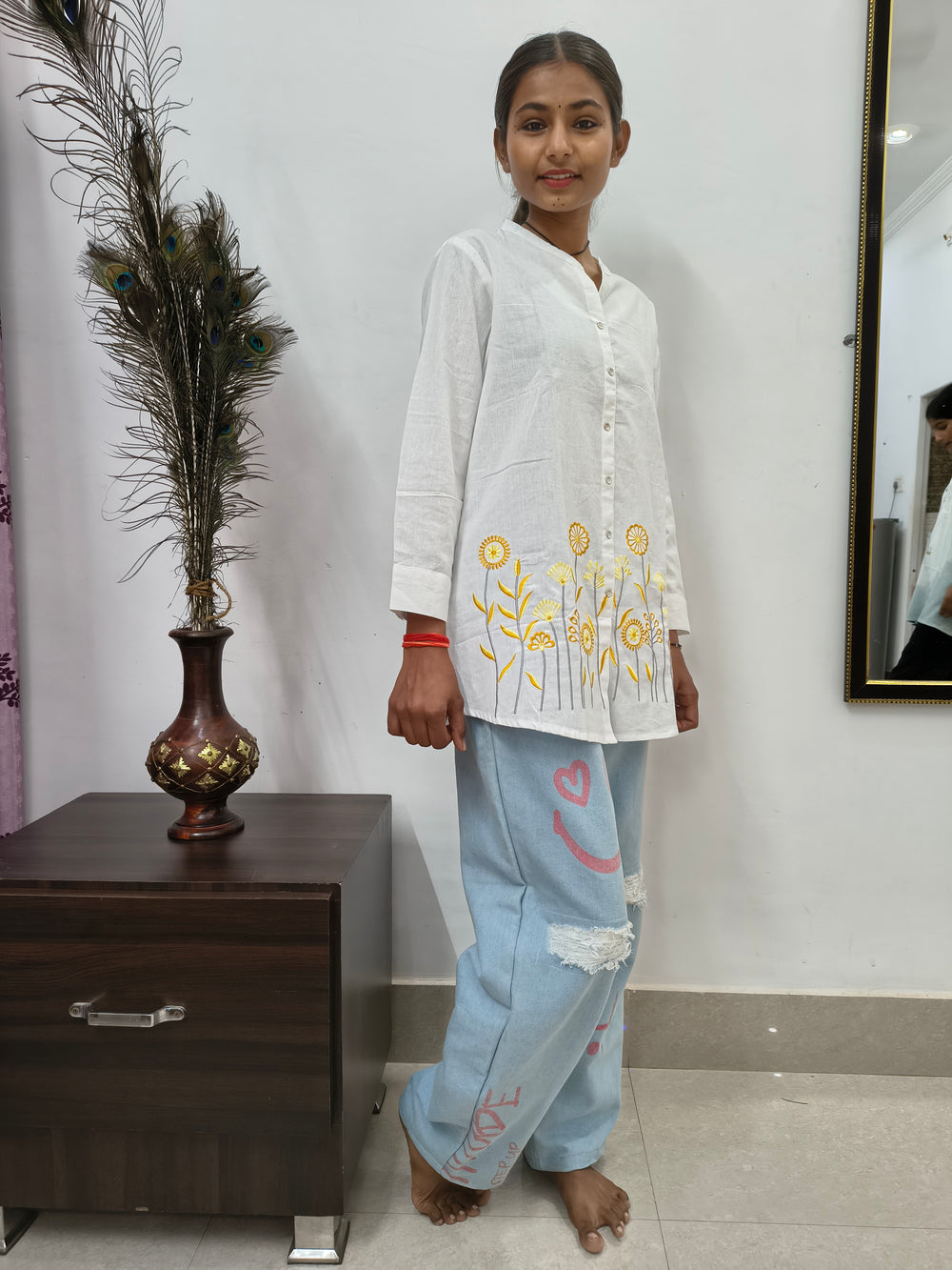 Model wearing white cotton short kurti with yellow floral embroidery and button-down front standing indoors