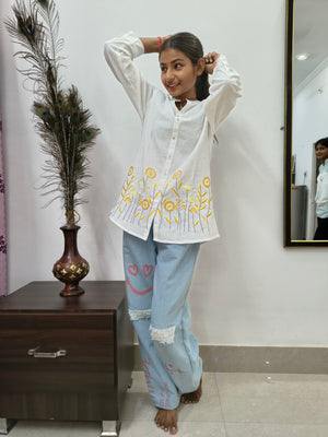 Model wearing white cotton short kurti with yellow floral embroidery and button-down front standing indoors