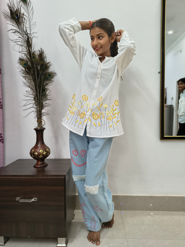 Model wearing white cotton short kurti with yellow floral embroidery and button-down front standing indoors