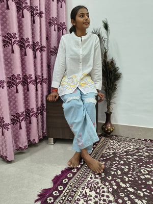 Model wearing white cotton short kurti with yellow floral embroidery and button-down front standing indoors