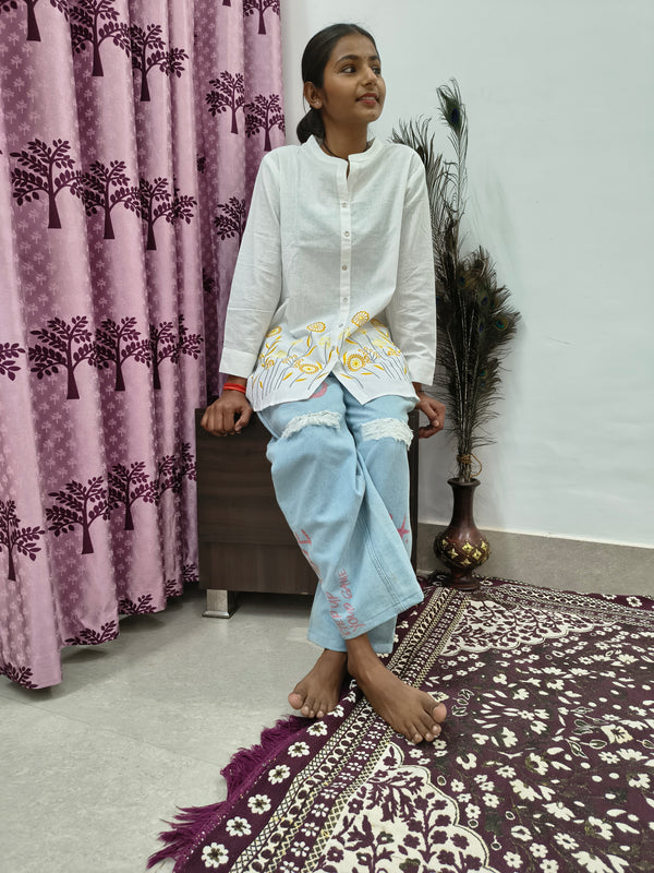 Model wearing white cotton short kurti with yellow floral embroidery and button-down front standing indoors