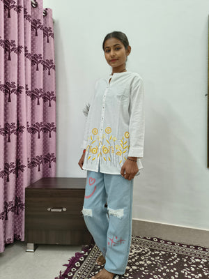 Model wearing white cotton short kurti with yellow floral embroidery and button-down front standing indoors