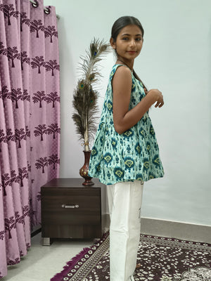 Woman wearing aqua blue tie dye sleeveless short cotton kurti standing indoors next to pink curtain