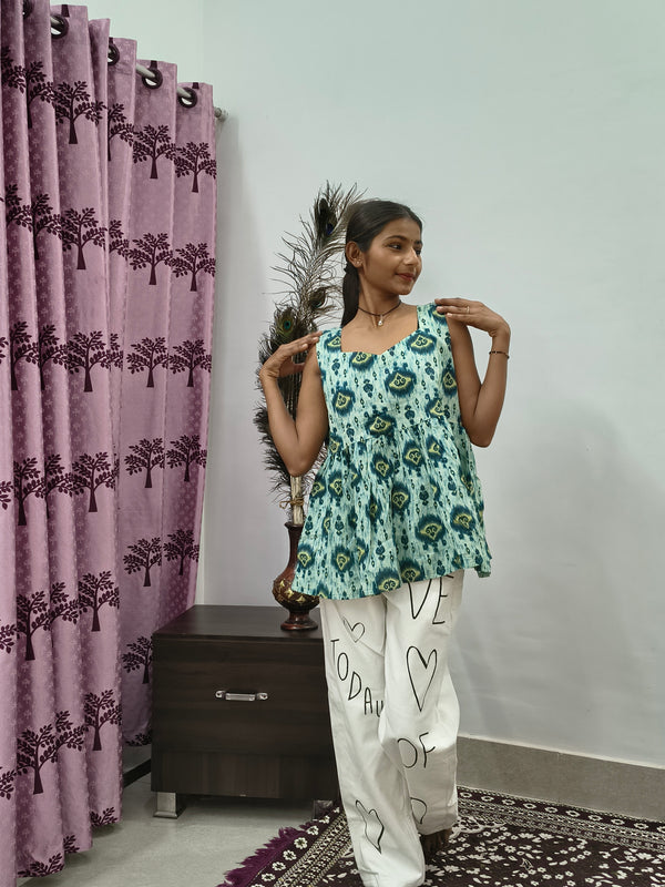 Woman wearing aqua blue tie dye sleeveless short cotton kurti standing indoors next to pink curtain