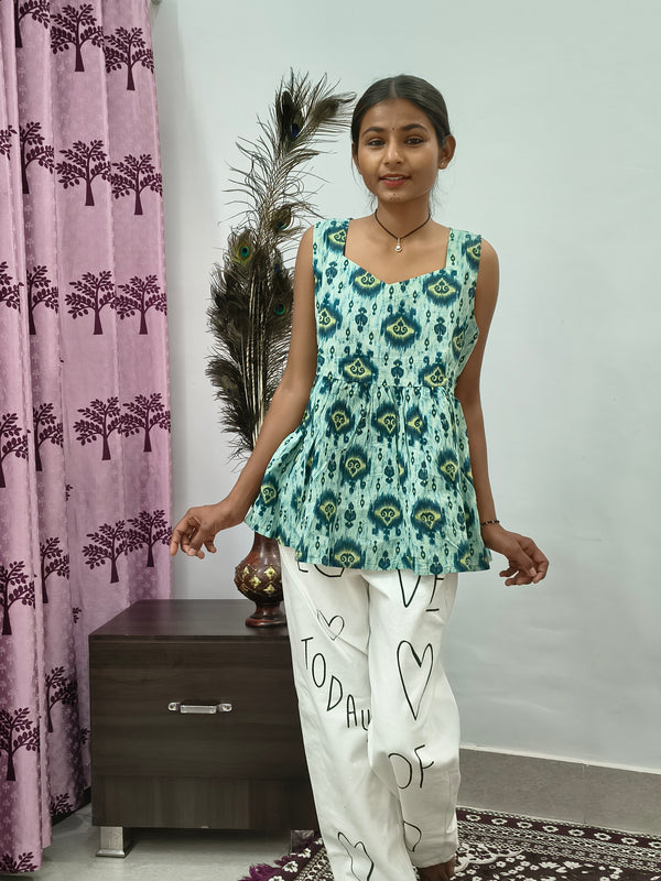 Woman wearing aqua blue tie dye sleeveless short cotton kurti standing indoors next to pink curtain