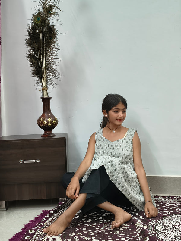 Woman wearing light grey floral print sleeveless short cotton kurti standing indoors