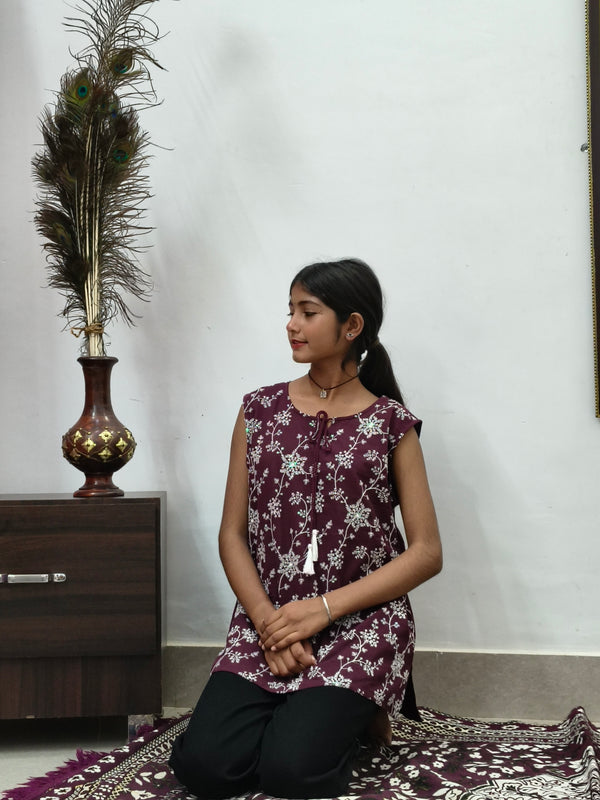 Woman wearing maroon floral print sleeveless short cotton kurti with tie-up neck standing indoors