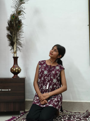 Woman wearing maroon floral print sleeveless short cotton kurti with tie-up neck standing indoors