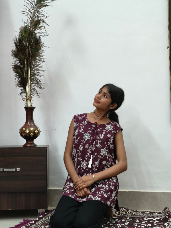 Woman wearing maroon floral print sleeveless short cotton kurti with tie-up neck standing indoors