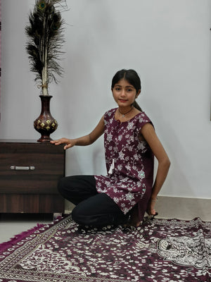 Woman wearing maroon floral print sleeveless short cotton kurti with tie-up neck standing indoors