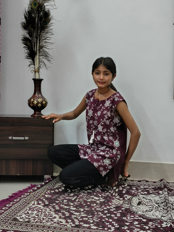 Woman wearing maroon floral print sleeveless short cotton kurti with tie-up neck standing indoors