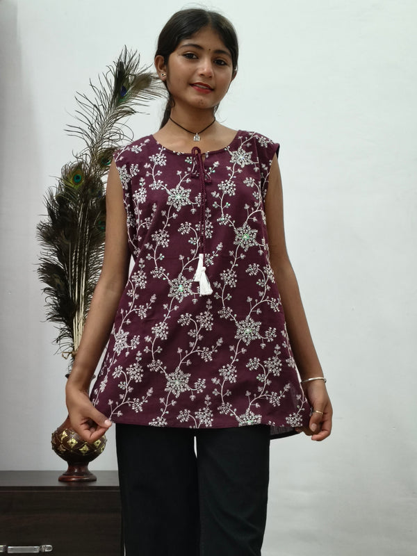 Woman wearing maroon floral print sleeveless short cotton kurti with tie-up neck standing indoors