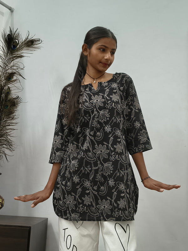 Model wearing black cotton short kurti with white floral vine print indoors