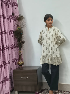 Model wearing ivory block print tiered short cotton kurti with gold motifs standing indoors