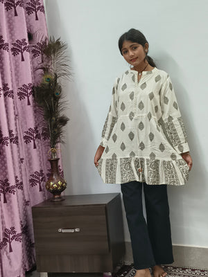 Model wearing ivory block print tiered short cotton kurti with gold motifs standing indoors
