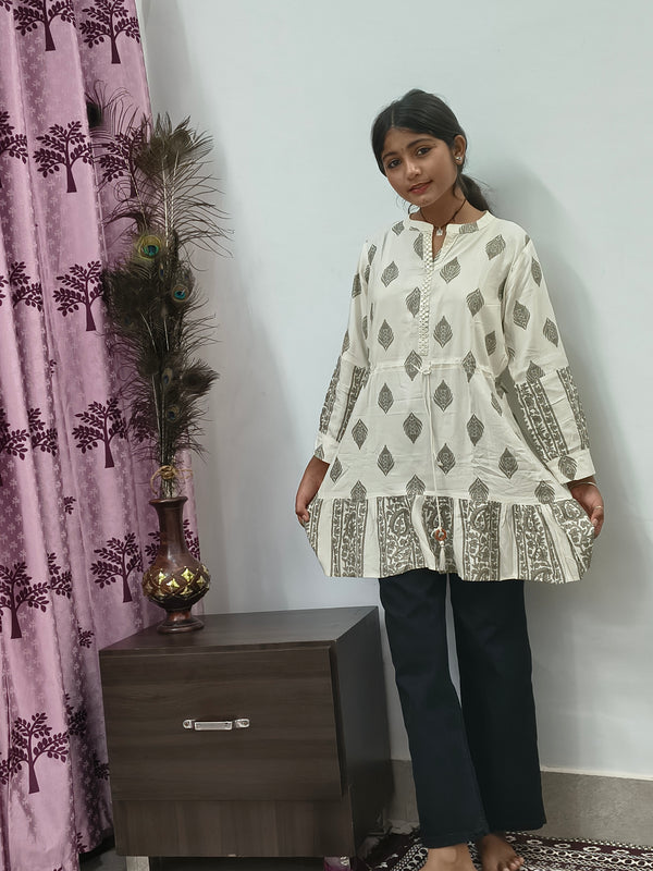 Model wearing ivory block print tiered short cotton kurti with gold motifs standing indoors