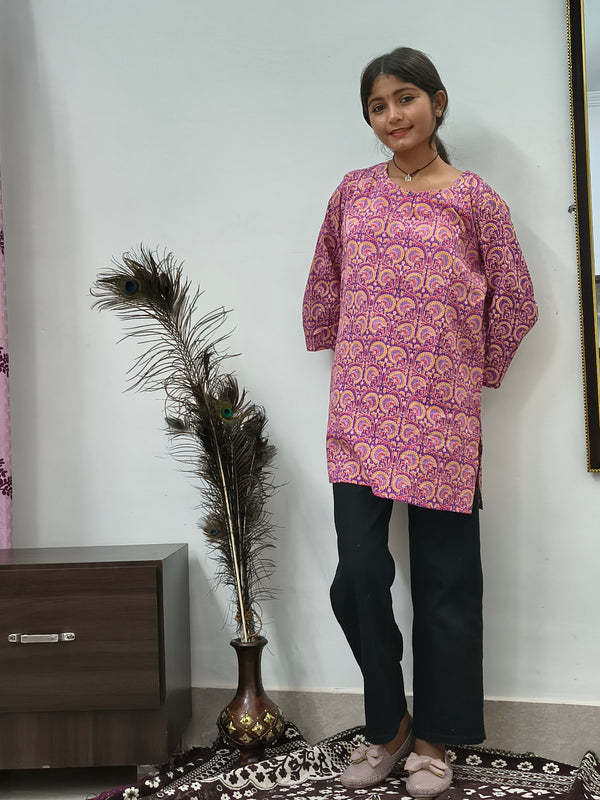 Model wearing purple cotton short kurti with paisley print standing indoors next to decorative feathers