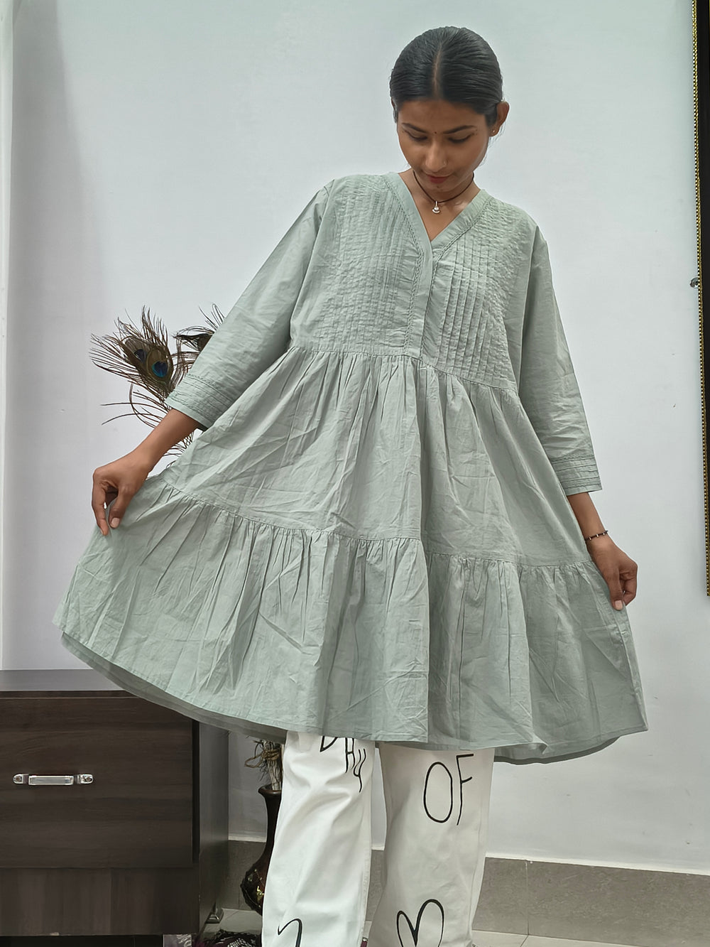 Model wearing sage green tiered cotton tunic kurti with v-neck and three quarter sleeves indoors