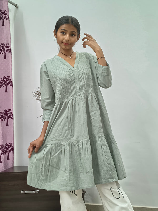 Model wearing sage green tiered cotton tunic kurti with v-neck and three quarter sleeves indoors