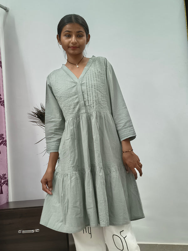 Model wearing sage green tiered cotton tunic kurti with v-neck and three quarter sleeves indoors
