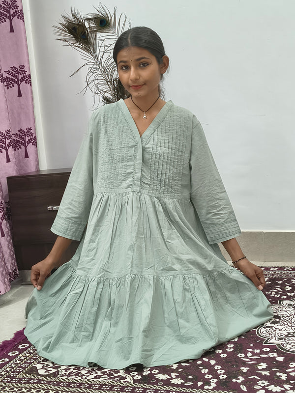 Model wearing sage green tiered cotton tunic kurti with v-neck and three quarter sleeves indoors