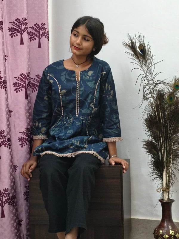 Woman wearing navy blue floral embroidered short cotton kurti with three quarter sleeves standing indoors