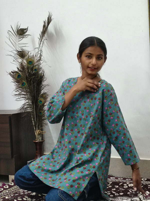 Model wearing teal green cotton short kurti with pink floral print and wide sleeves indoors