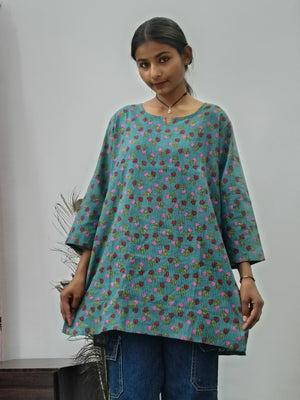 Model wearing teal green cotton short kurti with pink floral print and wide sleeves indoors