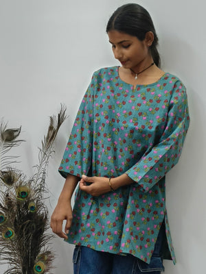 Model wearing teal green cotton short kurti with pink floral print and wide sleeves indoors