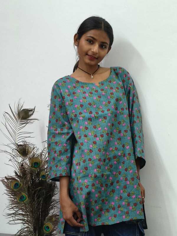 Model wearing teal green cotton short kurti with pink floral print and wide sleeves indoors