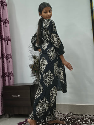 Woman wearing black cotton paisley print co ord set with cream motifs sitting indoors