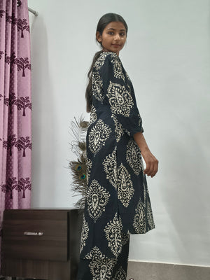 Woman wearing black cotton paisley print co ord set with cream motifs sitting indoors
