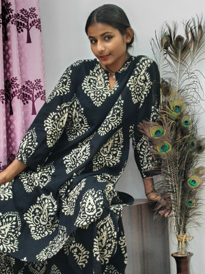 Woman wearing black cotton paisley print co ord set with cream motifs sitting indoors