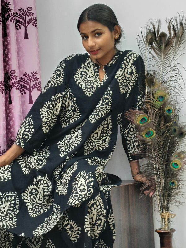 Woman wearing black cotton paisley print co ord set with cream motifs sitting indoors