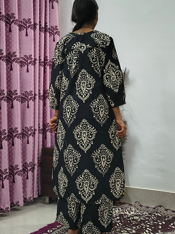 Woman wearing black cotton paisley print co ord set with cream motifs sitting indoors