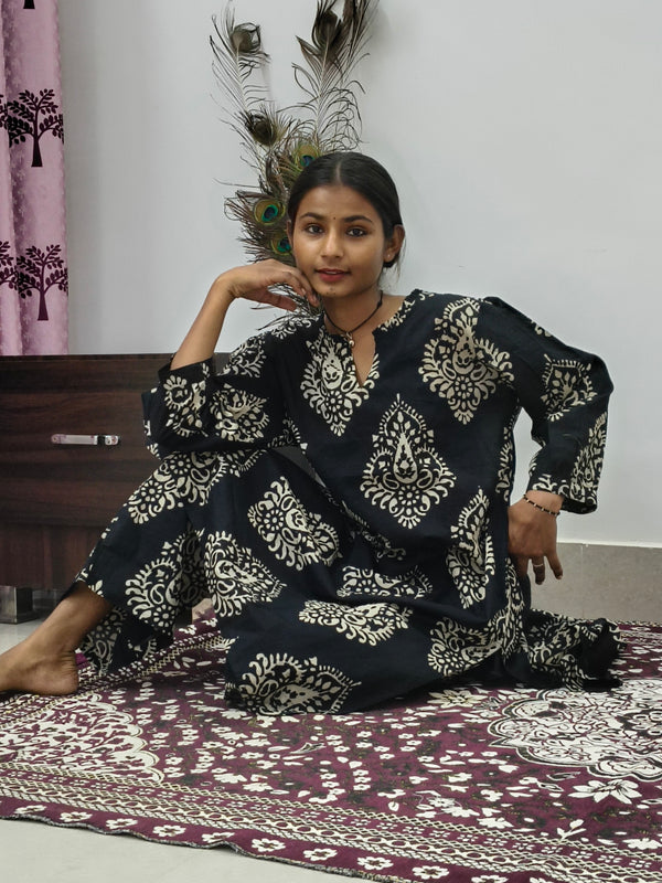 Woman wearing black cotton paisley print co ord set with cream motifs sitting indoors