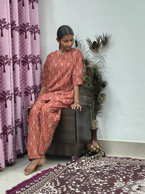 Woman wearing red mandala print cotton corset style kurta set with white block print palazzo pants in indoor setting
