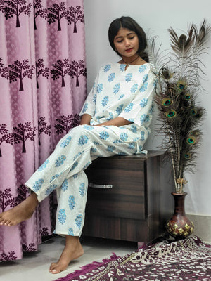 Woman wearing white and blue floral block print cotton kurta pajama set standing indoors with peacock feather decor