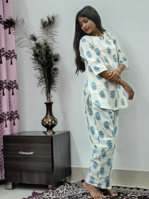 Woman wearing white and blue floral block print cotton kurta pajama set standing indoors with peacock feather decor